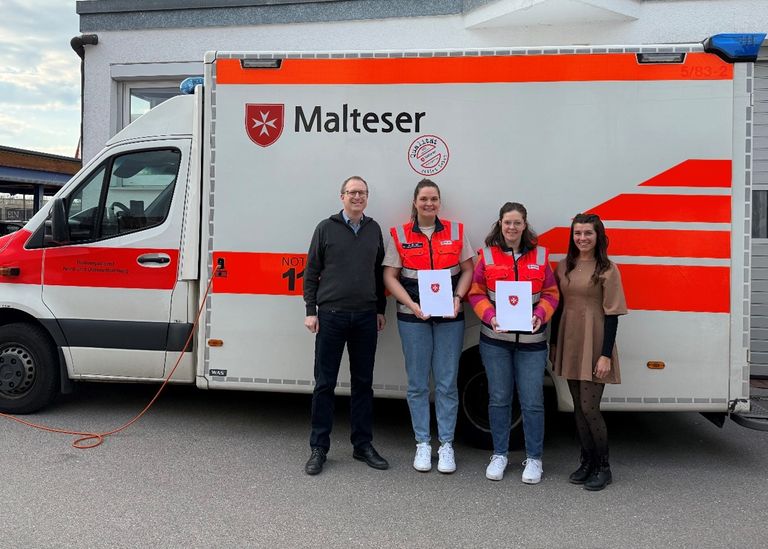 Die ausgezeichneten Malteser Helferinnen mit zwei anderen Maltesern vor einem Krankentransportwagen. 