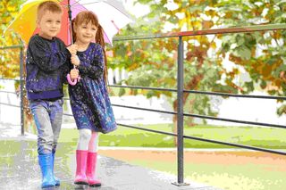 Zwei Kinder in Gummistiefeln mit Regenschirm