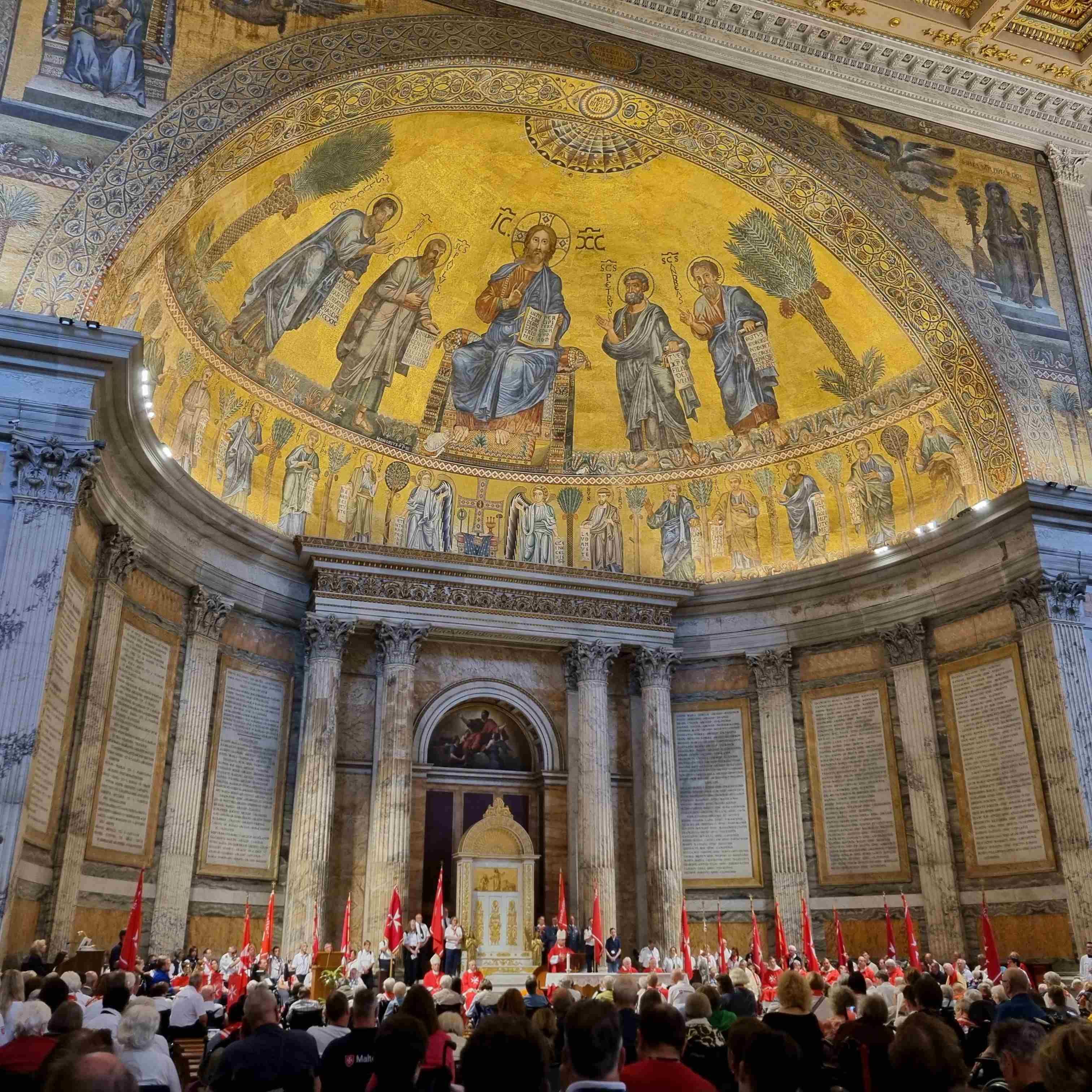 Innenraum einer Kirche mit goldener Mosaikdecke, Säulen und einer Menschenmenge im Vordergrund.