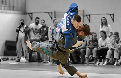 Zwei Judoka in farbigem Fokus bei einem Wurf, Zuschauer im Hintergrund schwarzweiß dargestellt.