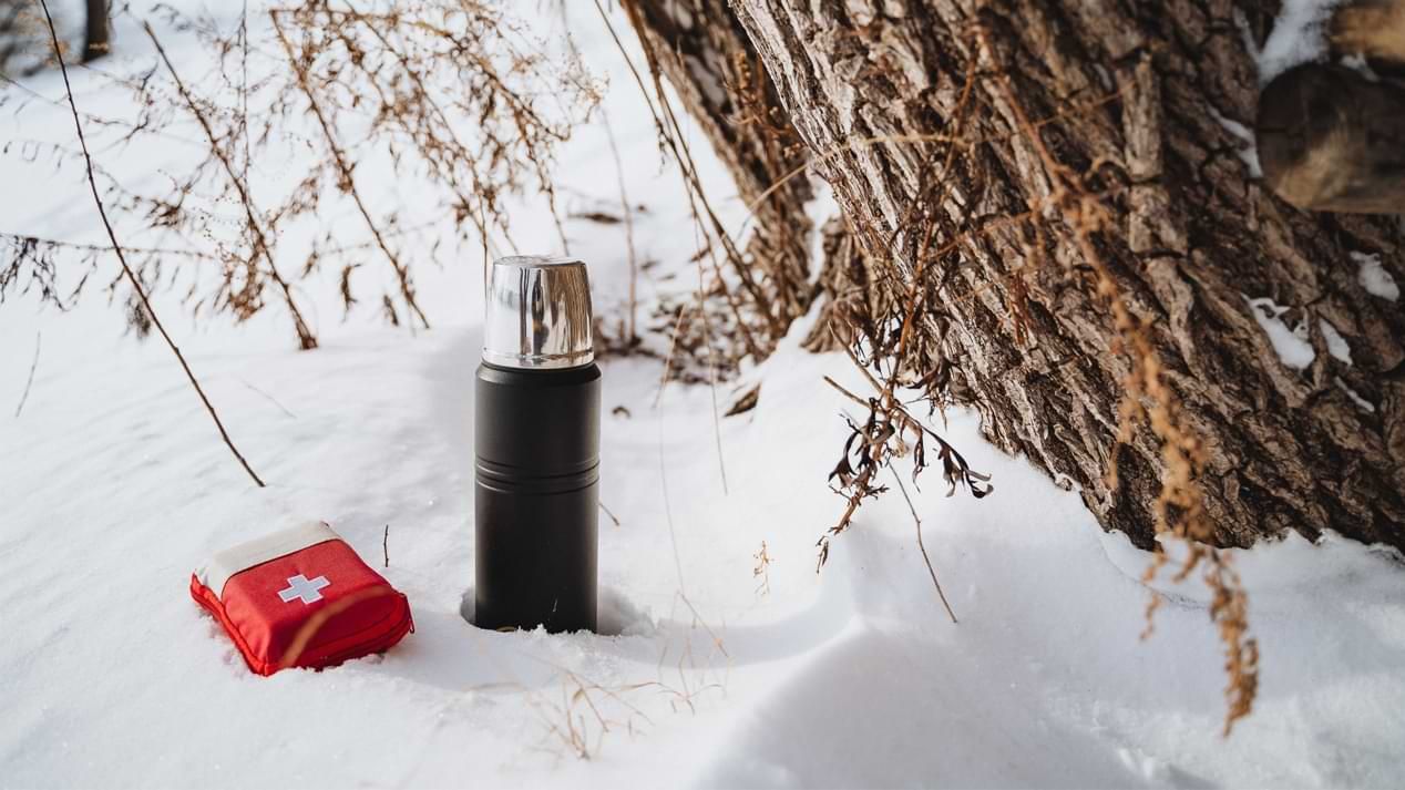 Ein Erste-Hilfe-Päckchen und eine Thermoskanne im Schnee.