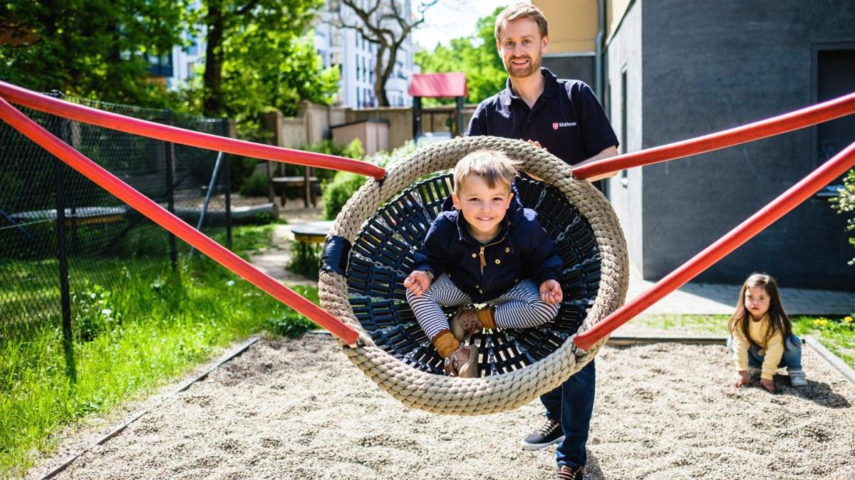 Ein Kind in einer Korbschaukel auf einem Spielplatz mit einem jungen Mann 