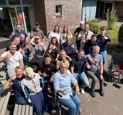 Eine Personengruppe sitzend und stehend in der Sonne. Alle recken den Daumen nach oben.