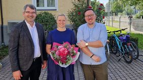 Ein Mann, eine Frau mit Blumenstrauß und ein weiterer Mann.