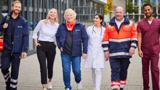 Malteser Mitarbeitende laufen gemeinsam durch den Innenhof eines Bürokomplexes.