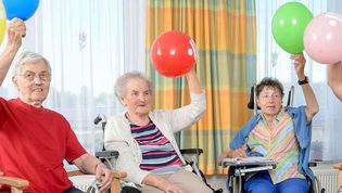 Ältere Menschen halten einen Luftballon in die Luft.