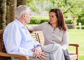 Eine jüngere Frau berät einen älteren Mann zur Patientenverfügung. Sie sitzen im Garten auf einer Bank.