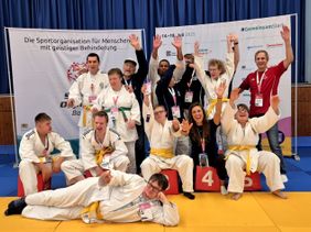 Judoteam von Menschen mit Behinderung jubelt nach Wettkampf gemeinsam auf der Matte.