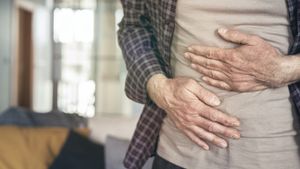 Hände umklammern den Bauch, sodass diejenige Person Schmerzen am Bauch hat.