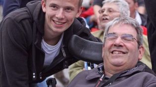 Junger Mann neben einem etwas älteren Mann im Rollstuhl. 