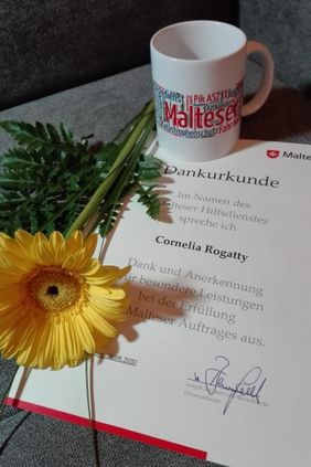 Auf einer Danke-Schön-Urkunde liegt eine Blume und steht eine Tasse.