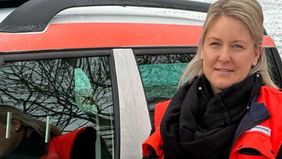 Eine Frau in Malteser Kleidung vor einem Malteser Dienstauto