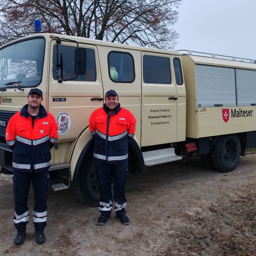 Zwei Malteser stehen vor einem historischen Einsatzwagen.