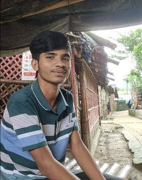 ein junger Mann sitzt und schaut in die Kamera. 