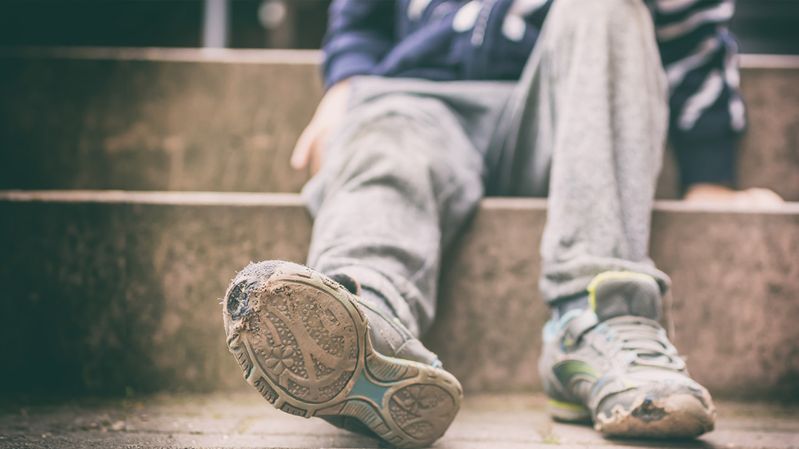 Ein junger Mensch auf einer Treppe mit alten, kaputten Turnschuhen