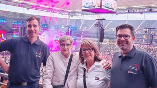 Zwei Helfer der Malteser und zwei Frauen stehen als Zuschauer bei einem Konzert