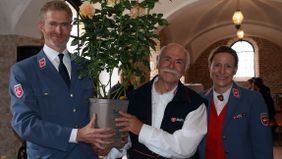 Der Malteser Diözesanleiter (links) und die Diözesanoberin (rechts) überreichen dem scheidenden ehrenamtlichen Geschäftsführer eine Topfpflanze 