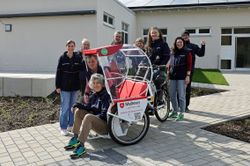 Mehrere Malteser Ehrenamtliche stehen draußen mit einer Fahrrad-Rikscha