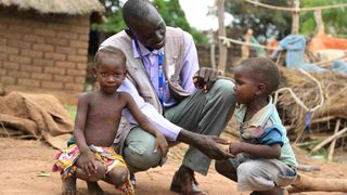 Ein Mitarbeiter für Malteser International unterhält sich mit zwei afrikanischen Kindern in ihrem Dorf.