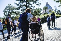 Eine Gruppe von Maltesern und Pilgern, zum Teil im Rollstuhl, laufen auf einem gepflasterten Weg durch den Vatikan.