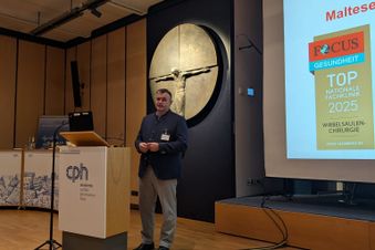 Mann hält einen Vortrag bei einer Veranstaltung, im Hintergrund ist eine Präsentation zu sehen.