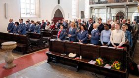 Menschen stehen in Kirchenbänken.