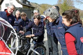 Malteser Ehrenamtliche sehen sich die Technik der Fahrrad-Rikscha an.
