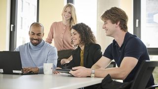 Malteser-Trainees bei einem Teammeeting am Tisch mit Laptop, engagiert und lächelnd in heller Büroumgebung