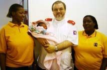 Father Gérard holding a newborn between two care workers.