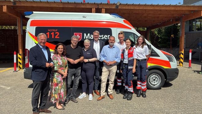 Mehrere Menschen stehen nebeneinander vor einem Malteser Rettungswagen