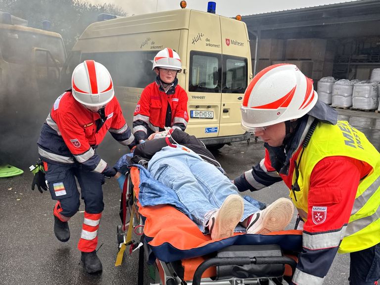 Ein qualmendes Auto, Jugendliche in Malteser Einsatzkleidung retten eine verletzte Person