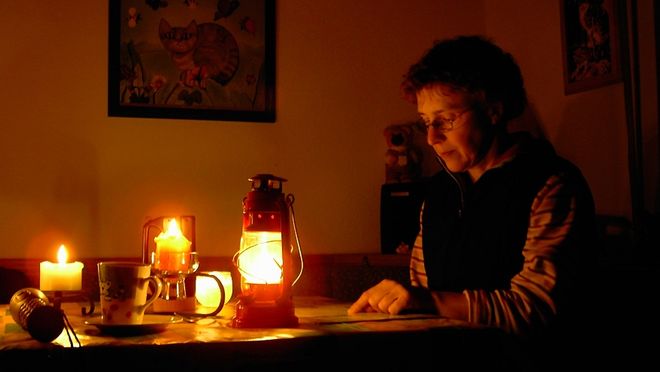 Eine Frau sitzt bei Kerzenschein und Laternen an einem Tisch und liest