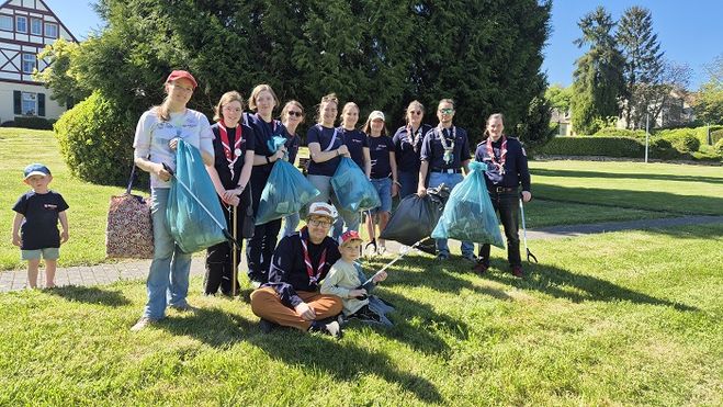 Gruppenfoto mit insgesamt 13 Kindern, Jugendlichen und ehrenamtlichen Gruppenleitungen, die 5 Müllsäcke hochhalten, die sie bei der Clean-Up Aktion gesammelt haben.