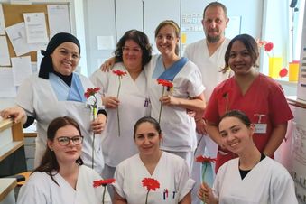 Pflegeteam mit roten Blumen in der Hand am Stationsstützpunkt versammelt.