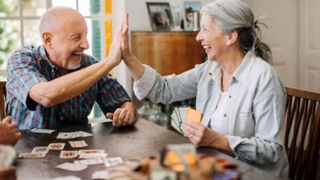 Ein ältere Mann und eine ältere Frau spielen Karten und klatschen sich lachend ab. 