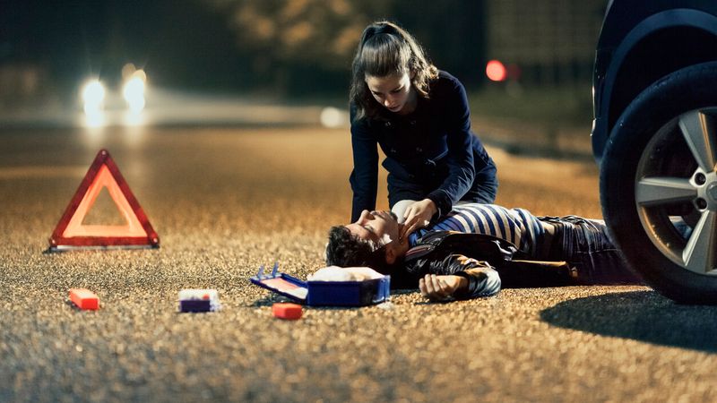 Erste Hilfe Autounfall: Junge Frau kniet über Unfallopfer und wendet Erste Hilfe Maßnahmen an