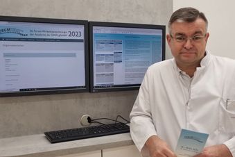 Arzt im weißen Kittel steht vor zwei Monitoren mit Infos zum Forum Wirbelsäulenchirurgie 2023.