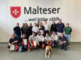 Auf dem Foto sind die Teilnehmenden des diesjährigen Einsatzsanitäterkurses zu sehen, vor dem Hintergrund des Malteser Logo