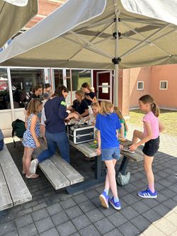 Kinder gemeinsam mit einer ehrenamtlichen Gruppenleitung an einer Button-Maschine, um Buttons zu erstellen.