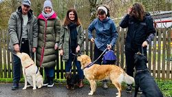 Fünf Menschen mit vier Hunden an der Leine stehen vor einem Zaun.