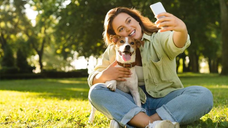 Eine lächelnde Frau in einem Park macht ein Selfie mit einem Hund.