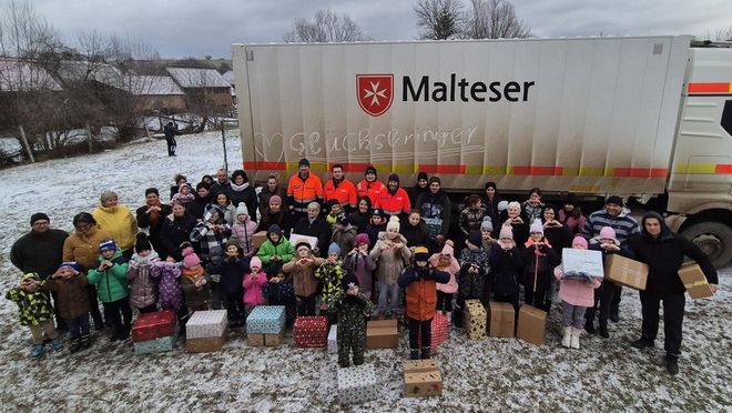 Viele Menschen stehen mit Paketen und vier Malteser Helfern vor dem Glücksbringer-LKW