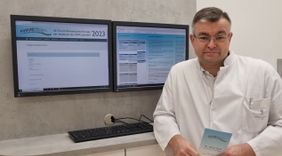 Arzt im weißen Kittel steht vor zwei Monitoren mit Infos zum Forum Wirbelsäulenchirurgie 2023.