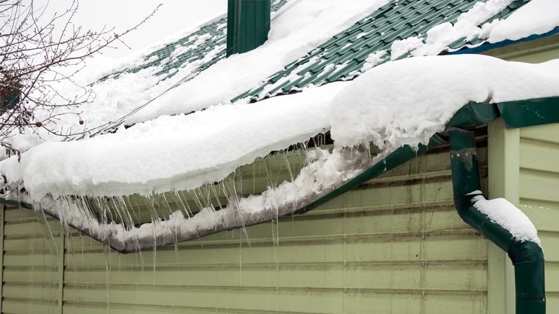 Eine Regenrinne, die unter der Last von Schnee und Eis verbogen ist.