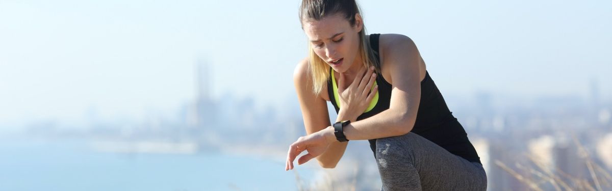 Junge Frau in Sportkleidung greift sich an die Brust und schaut auf eine Smartwatch 