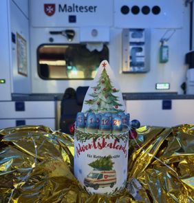 Ein selbst gebastelter Adventskalender für Rettungskräfte steht in einem Rettungswagen. Es handelt sich um eine Packung mit 24 Schokoriegeln. Auf jedem Schokoriegel befindet sind eine Banderole mit einem nummerierten Blaulicht und einer Du-Botschaft. 