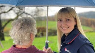 Malteser Mitarbeiterin hält einen Regenschirm über eine Seniorin