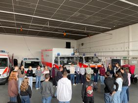 Auf dem Foto sind die Teilnehmenden der Ausbildung in der Fahrzeughalle der Mainzer Malteser zu sehen.