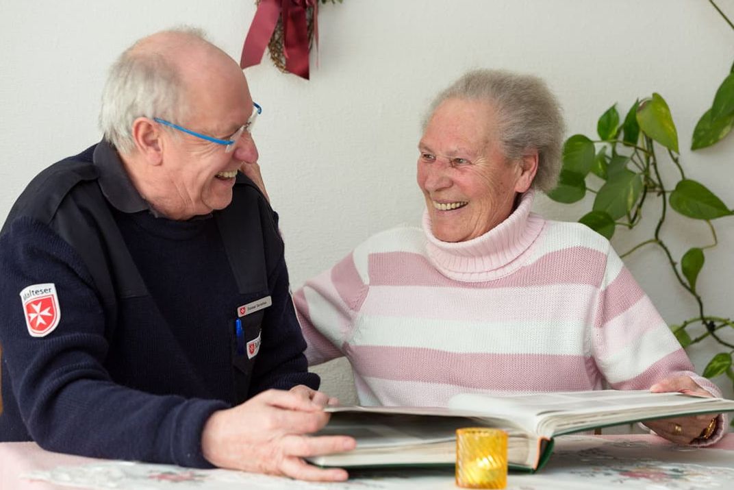 Malteser Mitarbeiter schaut sich mit Seniorin ein Fotoalbum an