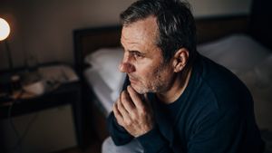 Ein älterer Mann sitzt in der Dunkelheit, nachdenklich auf seinem Bett.